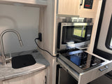This RV rental kitchenette features a modern sink, mounted microwave, and a space-saving pull-out induction cooktop.