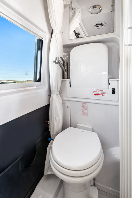 Compact RV rental wet bath with Dometic toilet, pull-out sink, and shower curtain, offering a clear view out the window.