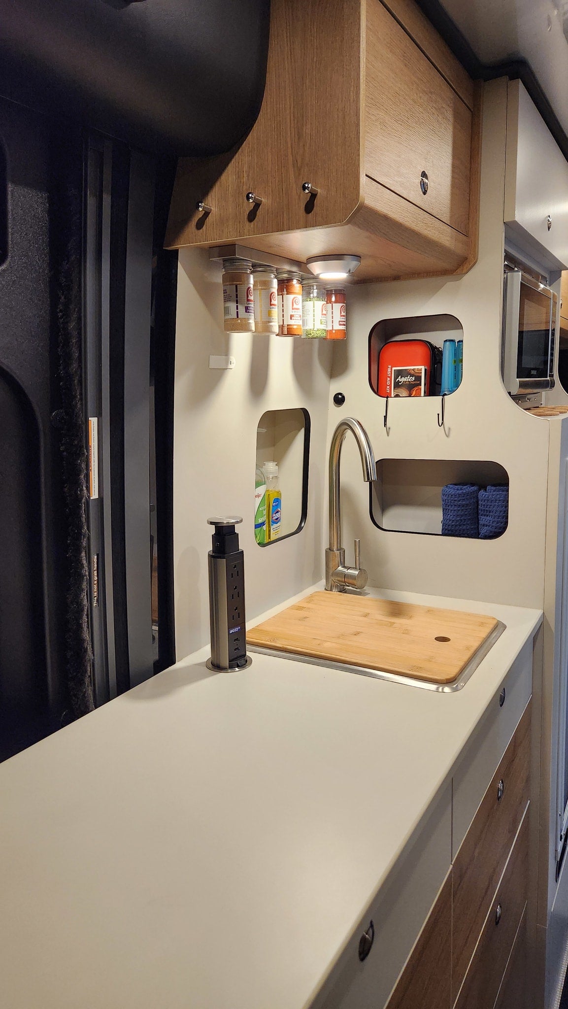 RV rental kitchen: compact design featuring a sink, pop-up outlet, overhead cabinets, and clever cubby storage. — photo 16