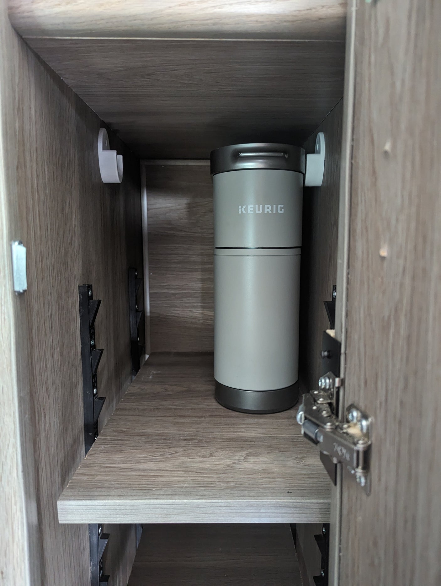 Keurig coffee maker in an RV rental cabinet, showing compact storage on an adjustable shelf.