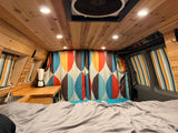 Inviting RV rental interior: wood-lined ceiling, comfy bed, mini kitchen, & vibrant retro curtains create a cozy space.