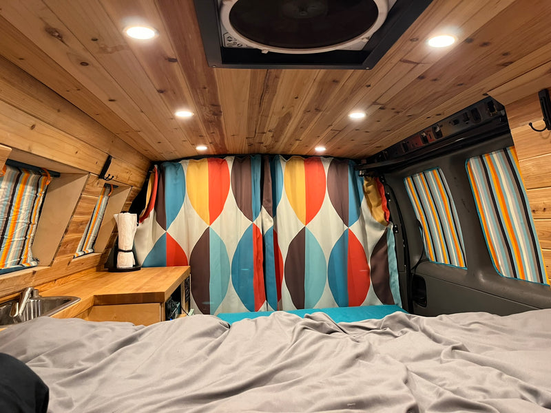 Inviting RV rental interior: wood-lined ceiling, comfy bed, mini kitchen, & vibrant retro curtains create a cozy space. — photo 7
