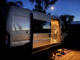 A cozy **rv rental** camper van, illuminated inside with an open door, rests under a serene crescent moon at night, perfect for **camping** adventures.