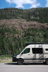 An RV rental camper van parked on a road with a dense, tree-covered mountain backdrop, perfect for outdoor adventure.