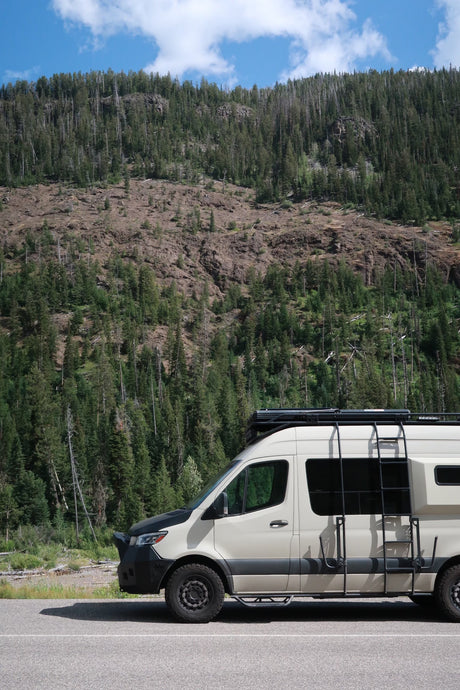 An RV rental camper van parked on a road with a dense, tree-covered mountain backdrop, perfect for outdoor adventure.
