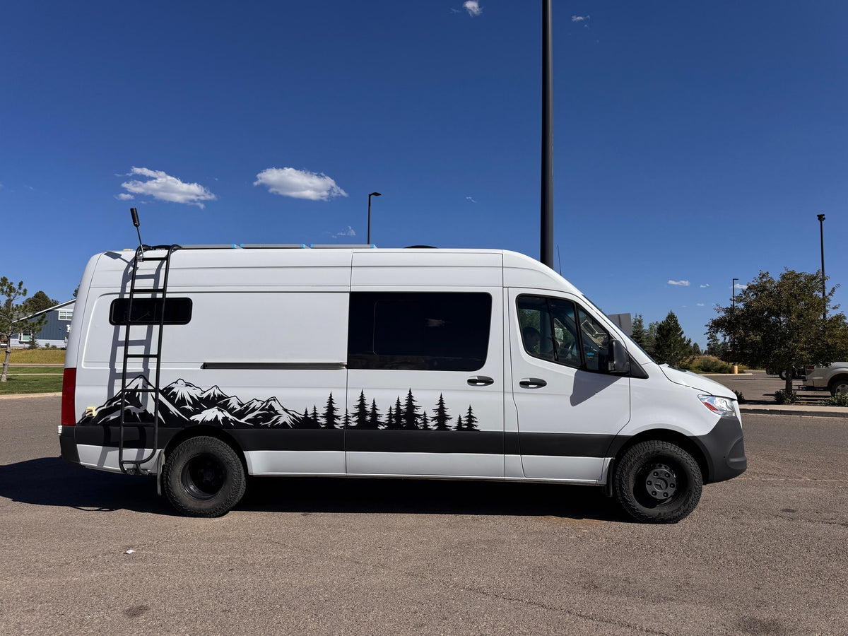 A white camper van with mountain and tree decals, an ideal rv rental for outdoor adventures under a clear blue sky.