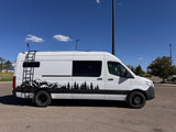 A white camper van with mountain and tree decals, an ideal rv rental for outdoor adventures under a clear blue sky.