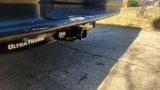 Close-up of a vehicle's rear bumper and Ultra Frame trailer hitch receiver, ideal for an RV rental. Concrete driveway visible.