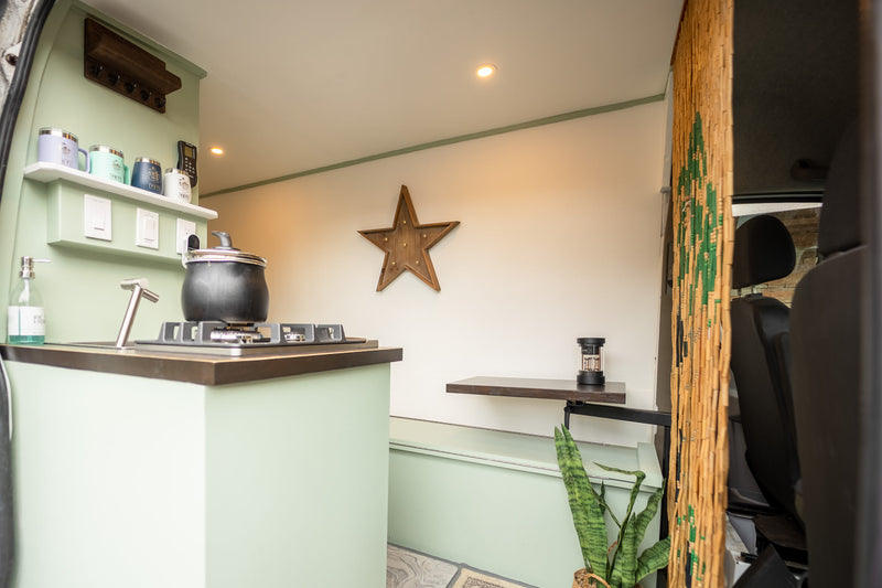 Cozy RV rental interior with light green kitchenette, stove, sink, shelving, and a star decor. Built-in table and plant add comfort. — photo 5