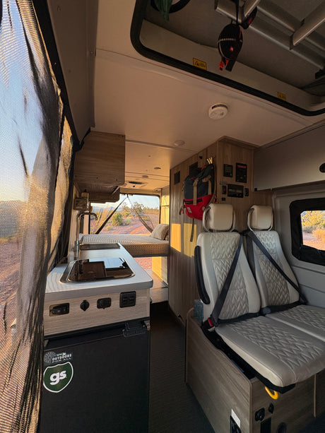 Spacious RV rental interior with kitchen, bed, and passenger seats, offering desert views through the open rear doors.