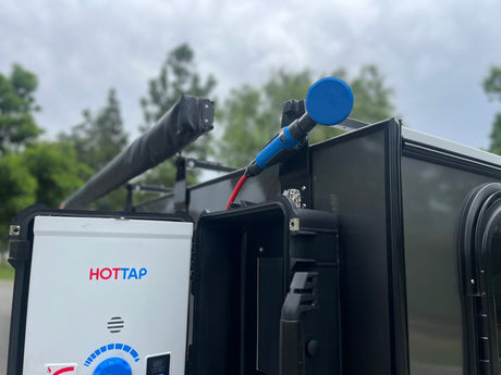 HOTTAP portable water heater & blue shower head mounted on an RV rental, ready for refreshing outdoor showers under a cloudy sky.