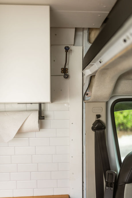 RV rental interior: white kitchen cabinet, subway tile backsplash, paper towels, decorative hook & passenger seatbelt.
