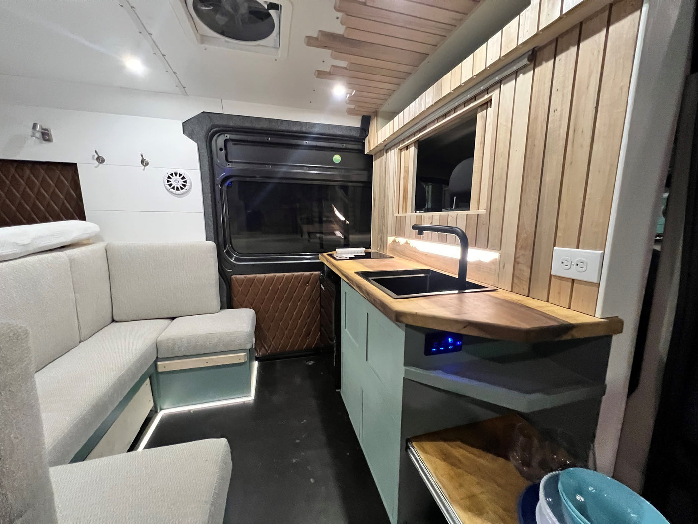 Modern RV rental conversion: L-shaped sofa, full kitchen with sink/cooktop, ambient lighting. Ideal for road trips.