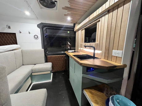 Modern RV rental conversion: L-shaped sofa, full kitchen with sink/cooktop, ambient lighting. Ideal for road trips.