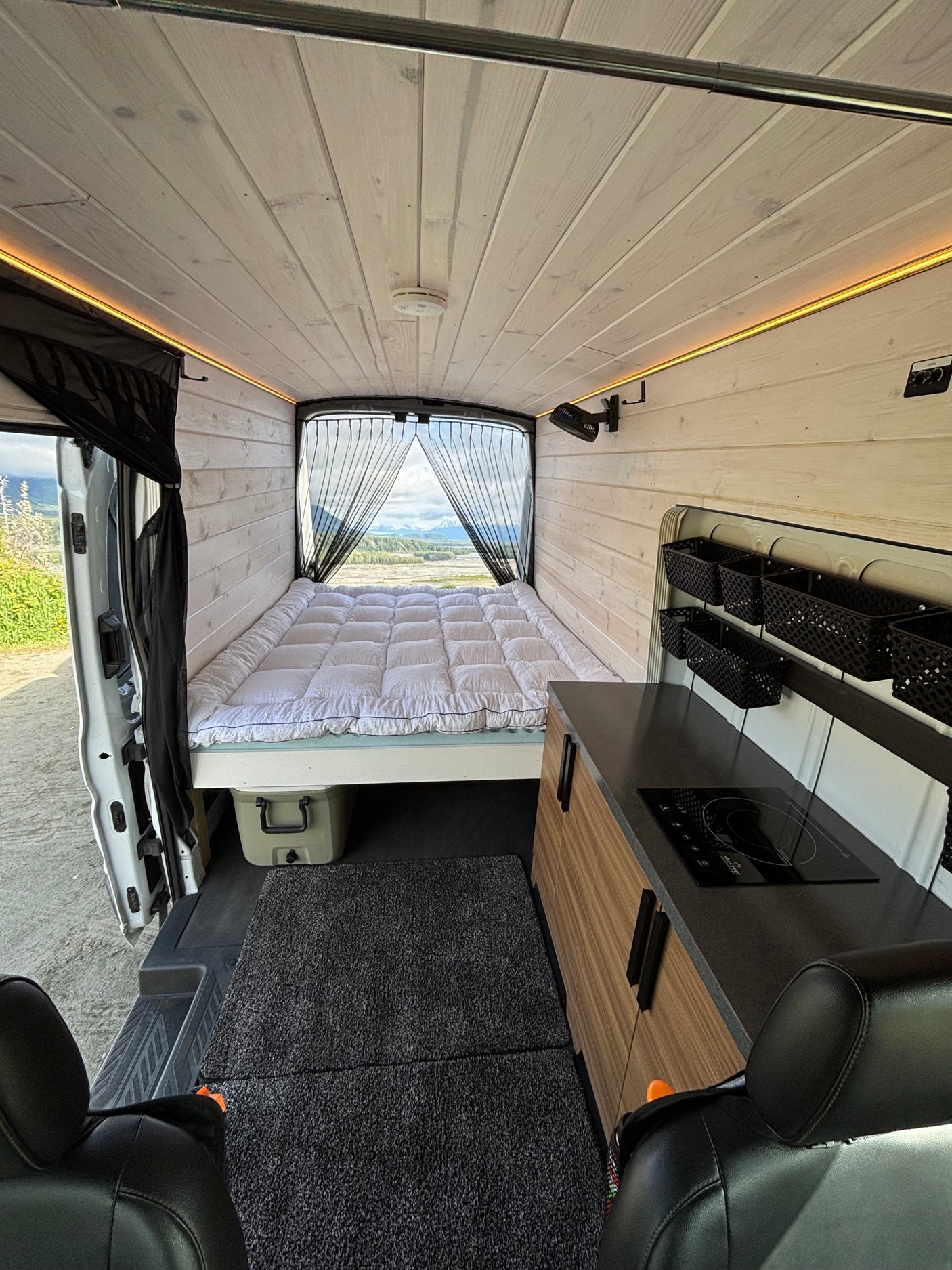 Spacious camper van interior for your next rv rental adventure, featuring a comfy bed, kitchen, & mountain views.