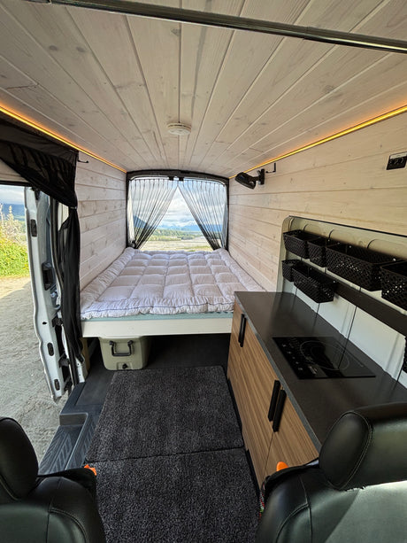 Spacious camper van interior for your next rv rental adventure, featuring a comfy bed, kitchen, & mountain views.