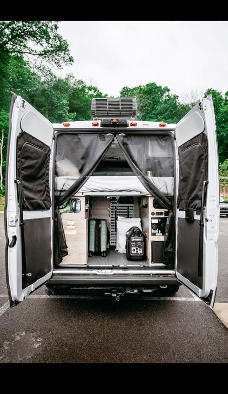 Open rear of a white RV rental camper van, showing a bed, organized storage, suitcases, and power station inside.