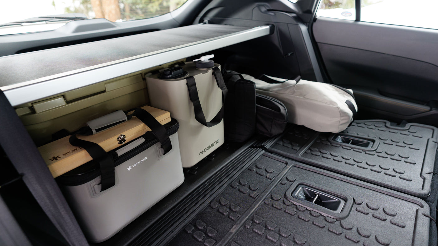 Organized RV rental trunk with Dometic jug, Snow Peak cooler, and mats for camping gear.