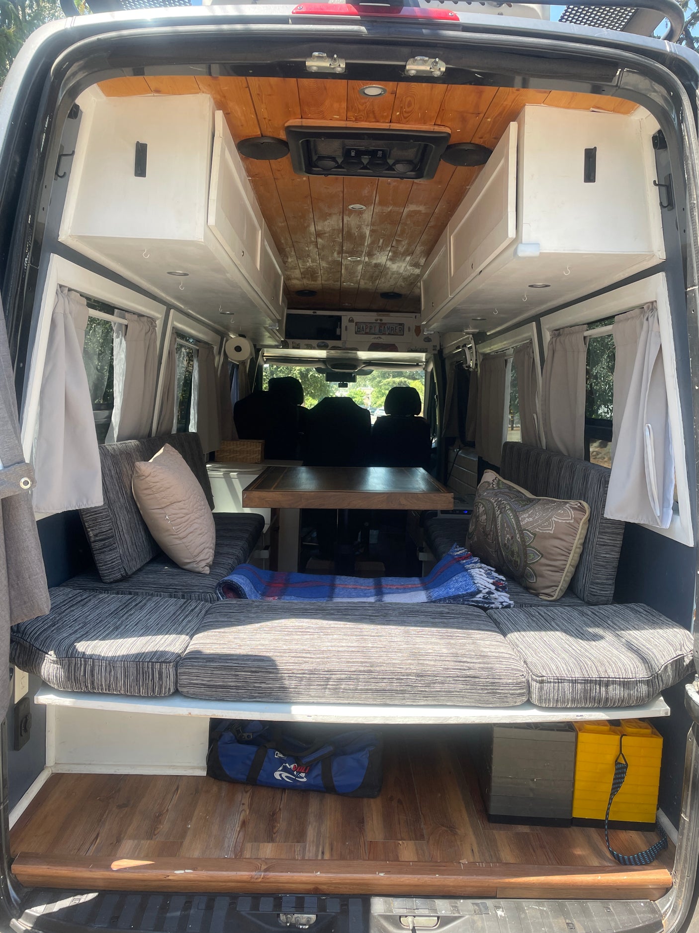 RV rental interior from the rear: wood ceiling, white cabinets, gray cushioned benches, central table, and under-seat storage.