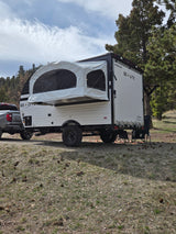 Go > Lite pop-up RV rental ready for off-road camping with a truck, surrounded by trees and pine cones.