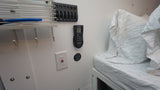 Inside an RV rental: Bed with striped sheets, wall-mounted AC remote, power panel, and storage hooks offer convenience.