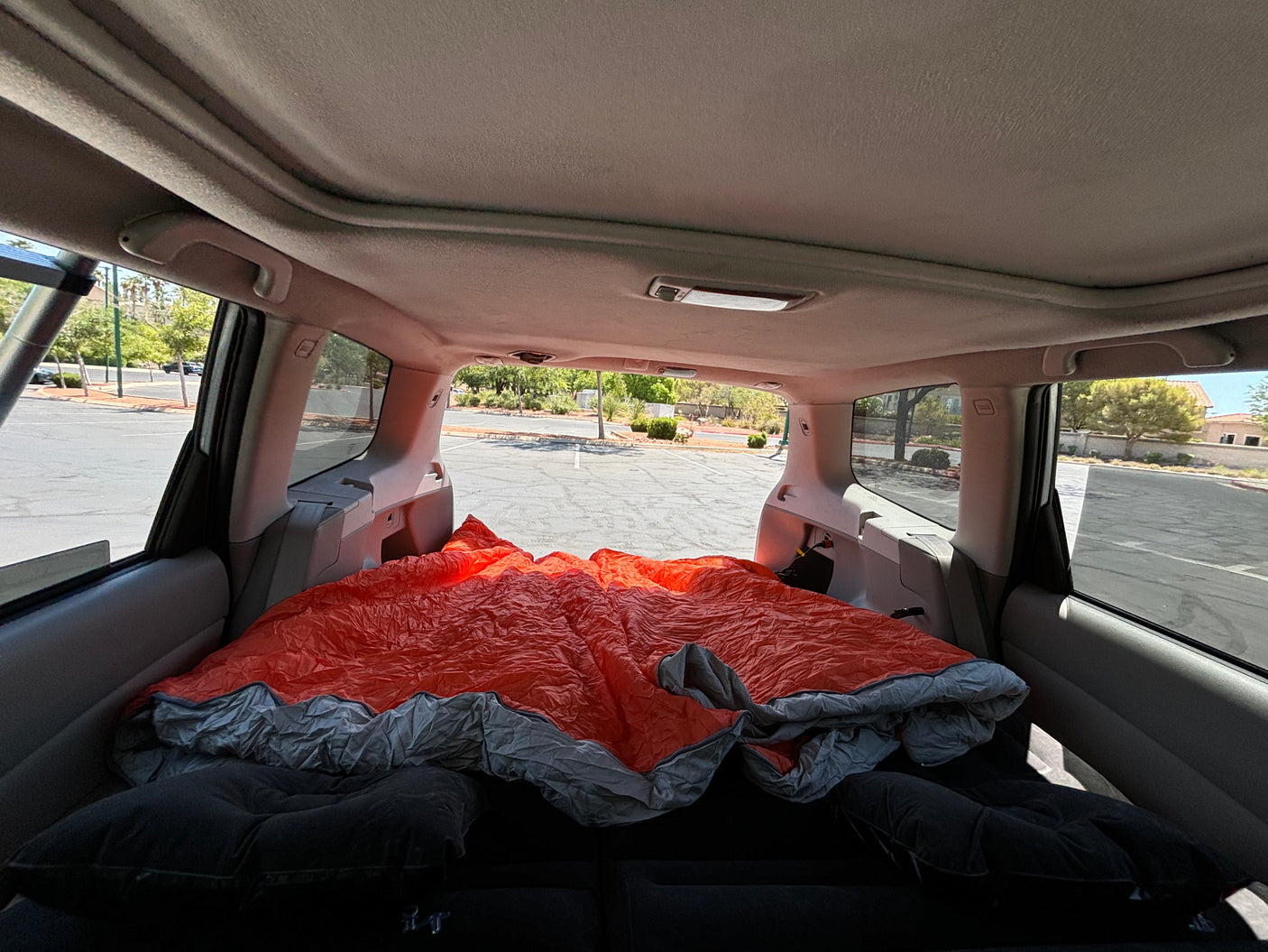 A car's interior transformed into a cozy sleeping space for camping, complete with a bright orange sleeping bag. Your RV rental alternative!