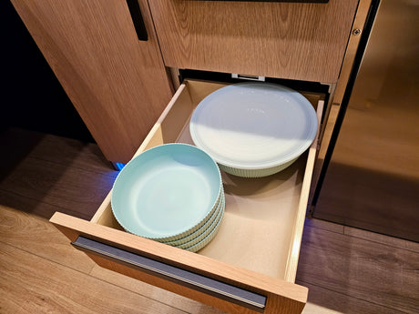 Inside an RV rental, an open kitchen drawer reveals light blue dishes and a lidded bowl, perfect for compact storage.