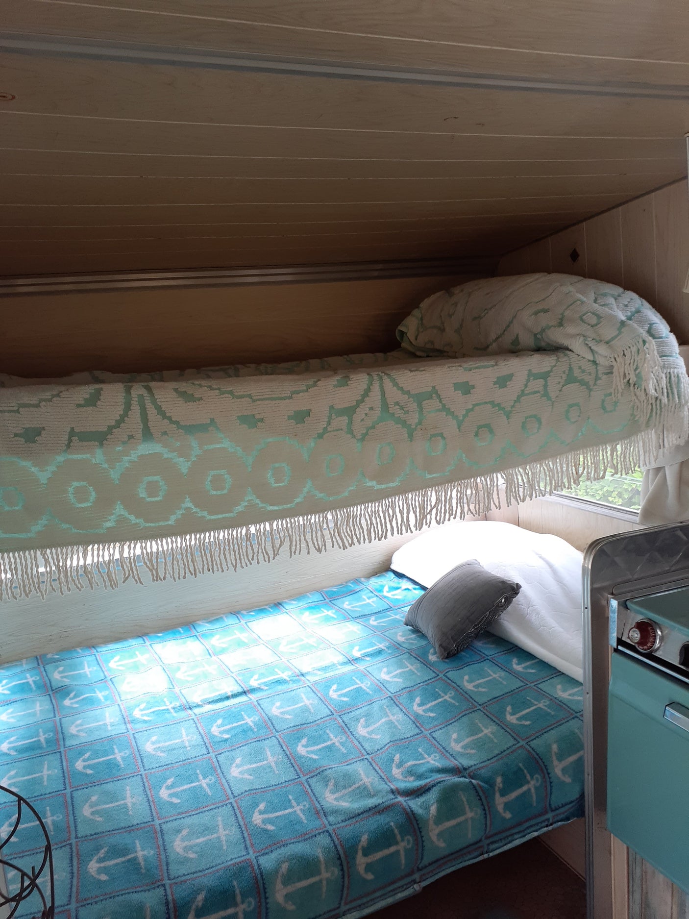 Cozy RV rental interior with a blue anchor blanket, patterned throw, and compact kitchen area.