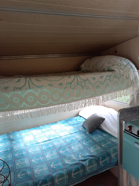 Cozy RV rental interior with a blue anchor blanket, patterned throw, and compact kitchen area.