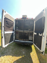 Back view of an RV rental camper van with open doors, revealing a cozy bed, storage, and bug screen. Ideal for van life adventures.