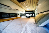 Inside a modern RV rental: a cozy bed, kitchen, and front cabin area. Ready for your road trip comfort.