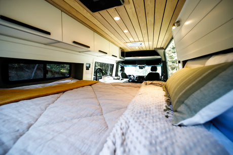 Inside a modern RV rental: a cozy bed, kitchen, and front cabin area. Ready for your road trip comfort.