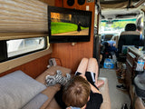 In this RV rental, a child relaxes watching a movie, possibly Harry Potter, with a plush zebra.