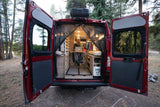Your ultimate mobile office awaits! See a woman working in an RV rental camper van parked in a serene forest.