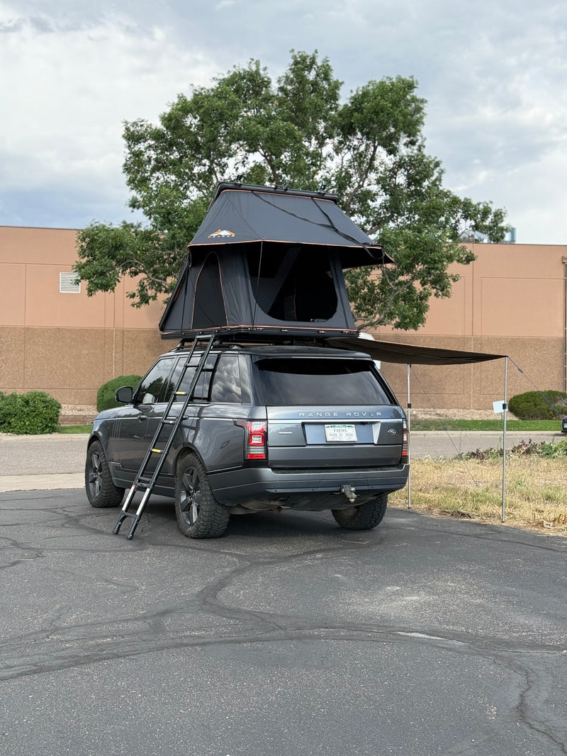 A charcoal Range Rover with a deployed rooftop tent, ladder, and side awning, set up for camping. A unique RV rental alternative. — photo 9