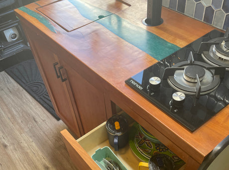 Stylish RV rental kitchen: custom wood/resin counter, gas stove, stocked drawer with dishes. Ideal for your trip!