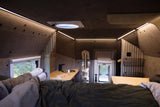 Cozy rv rental interior: bed, compact kitchen with sink, heater, and ambient LED lighting. Feet relaxing by the window.