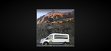 White Wandervans rv rental van on a scenic mountain road, ready for rugged terrain adventures.