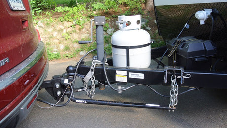 RV rental trailer's complete towing setup: hitch, safety chains, propane tanks, battery, and weight distribution bars.