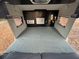 Cozy RV rental bedroom with large bed, wall AC unit, storage, and scenic window views. Perfect for travel.