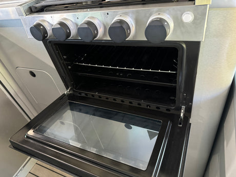 This RV rental kitchen features an open oven with racks and stove control knobs, showcasing its compact, stainless steel design.