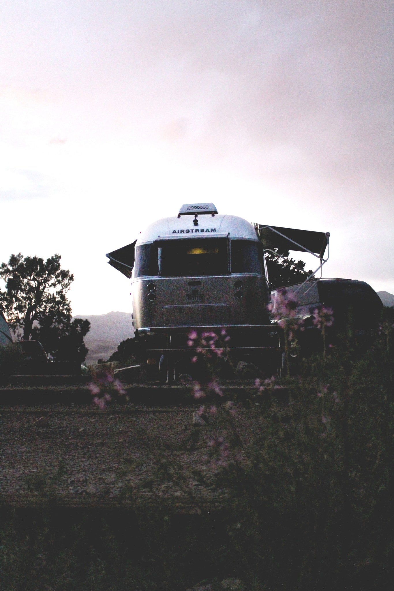  nestled among mountains and calm waters.|Discover adventure with an RV rental! A classic silver Airstream trailer is parked at dusk in a scenic outdoor setting — photo 2