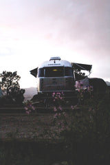 Discover adventure with an RV rental! A classic silver Airstream trailer is parked at dusk in a scenic outdoor setting, with flowers in the foreground.