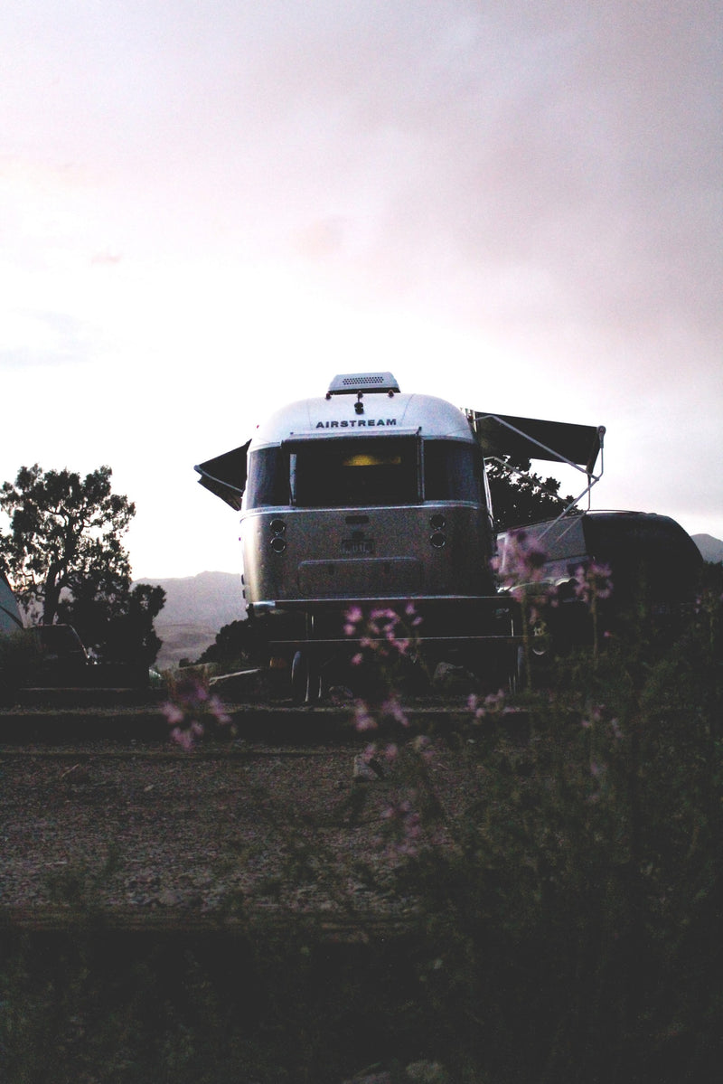  nestled among mountains and calm waters.|Discover adventure with an RV rental! A classic silver Airstream trailer is parked at dusk in a scenic outdoor setting — photo 2