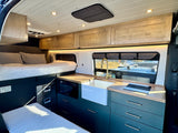 Modern RV rental interior with a cozy bed, stylish kitchen featuring a sink and cooktop, and ample storage.