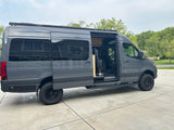 This RV rental is a grey Mercedes Sprinter camper van with an open side door, showcasing its custom interior and off-road tires.