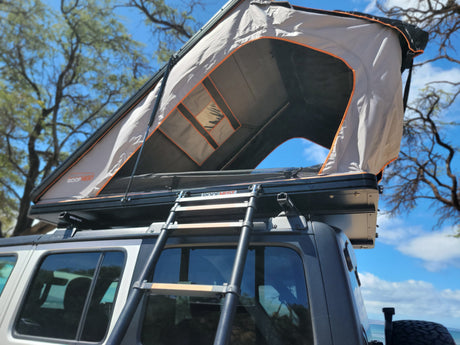 An open grey Roofnest rooftop tent sits on an RV rental vehicle with its ladder extended. Ready for a camping adventure.