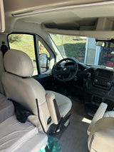 Inside a modern **rv rental**: view of the bright driver's cabin, dashboard, steering wheel, and front seats with an adjacent bed.