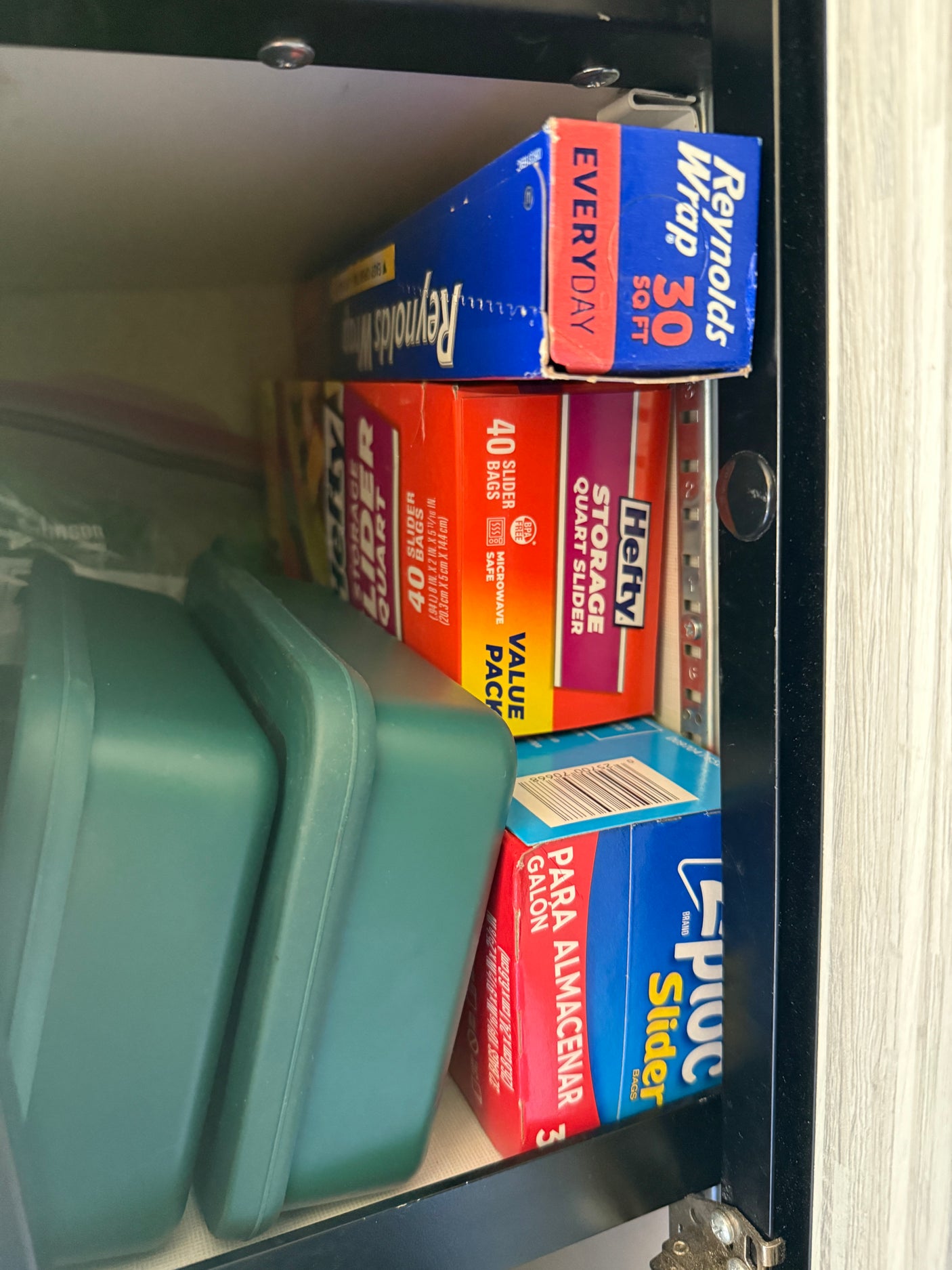 RV rental kitchen cabinet with organized food storage: Reynolds Wrap, Hefty, Ziploc bags, and green containers.