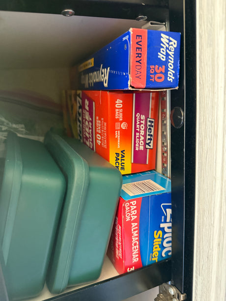 RV rental kitchen cabinet with organized food storage: Reynolds Wrap, Hefty, Ziploc bags, and green containers.